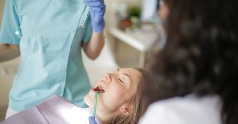 Whiten Teeth - Crop faceless female dentist in uniform holding mouth mirror while preparing for inspecting female patient teeth with assistant holding tube suction in patient mouth