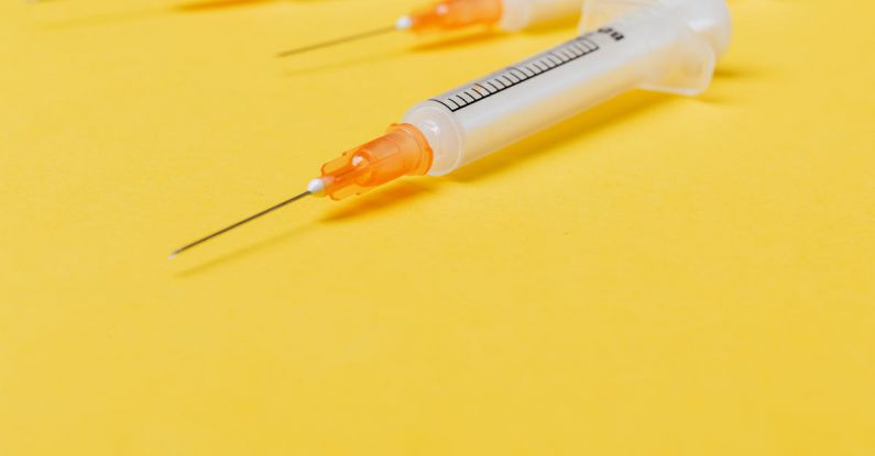 Plastic Use - Medical single use disposable syringe without protective cover on needle and with empty barrel placed on bright yellow surface