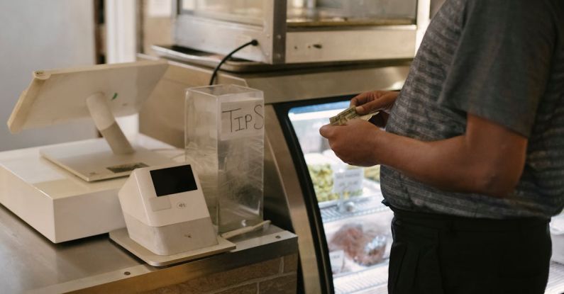 Grocery Bills - Unrecognizable male in casual clothes standing with money near cash register in grocery store while making purchase near glass showcase