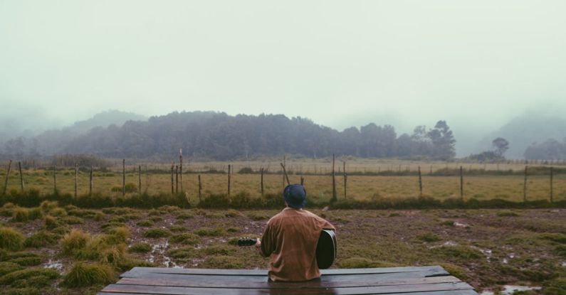 Traveling Solo - Person Holding Guitar Sitting on Brown Wooden Balcony