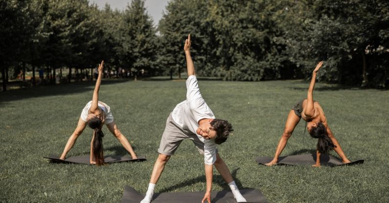 Healthy Lawn - Group of diverse friends doing Revolved Wide Legged Forward Bend while exercising yoga on lawn